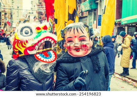 Two people wearing traditional Chinese masks, Big Head Doll and Lion, walking on street in Chinatown, Downtown of Manhattan, New York, celebrating Chinese New Year. Instagram filtered look.