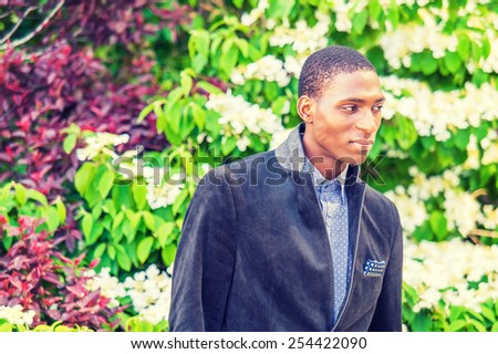 Day Dream. A young black college student standing outside by green, purple, white plants, looking down, thinking, making funny face, smiling. Concept of teenager self esteem. Instagram filtered look.