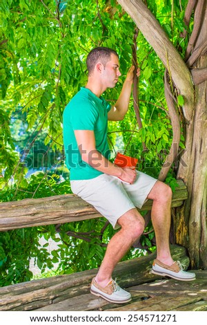 Thinking after reading. Wearing short sleeve shirt, shorts, leather casual shoes, holding red book, a young guy sitting on tree trunk, thinking. Concept of introspection, self questioning, examination
