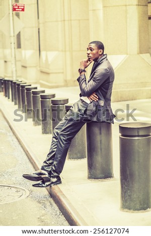 Thinking Outside. Young black college student sitting on street, hunchbacked, hand touching his chin, crossing legs. Concept of teenagers questioning life, career, self esteem. Retro filtered look.