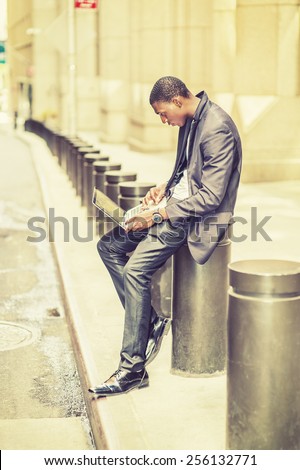 Working anywhere, anytime. A young black college student sitting on street, hunchbacked, reading Internet on a laptop computer. Concept of new technology in our daily life. Retro filtered look.