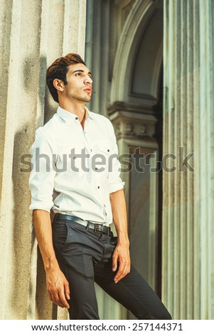 Portrait of Young Businessman. Wearing white shirt, black pants, sleeves rolling over, a young college student is standing outside an office building, looking up, thinking. Instagram filtered look.