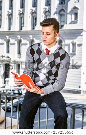 Man Reading Outside.  Dressing in black, white, gray patterned sweater, jeans, a young college student sitting on a railing outside, opening red book, looking down, reading, Instagram filtered look.