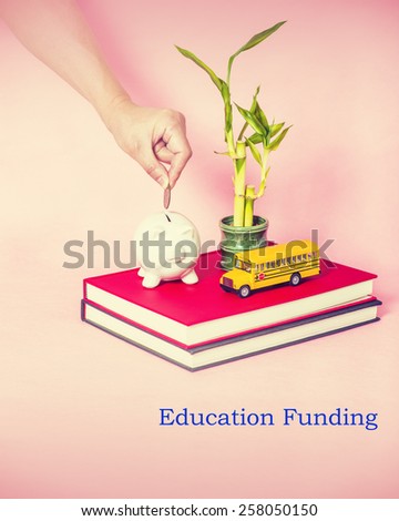 Books with school bus model, bamboo plants, piggy bank, a hand holding a coin. Concept of education funding, school funding, public supports and school growth. Instagram filtered look. Copy Space.