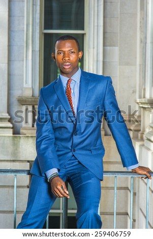 Businessman thinking outside. Dressing formally in blue suit,  patterned tie, a young black guy sitting on railing in vintage style office building, inclining shoulder,  thinking, lost in thought.