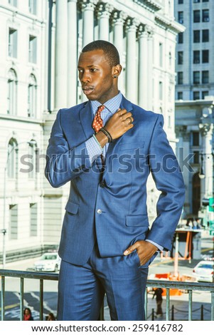Businessman thinking outside. Dressing in blue suit, a young black guy standing by railing in the front of vintage style office building, hand putting on shoulder, thinking. Instagram filtered look.