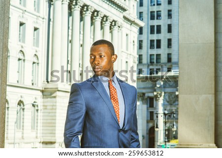 Portrait of successful businessman. Dressing in blue suit, a young black guy standing in the front of vintage style office building, looking away. Instagram filtered look.