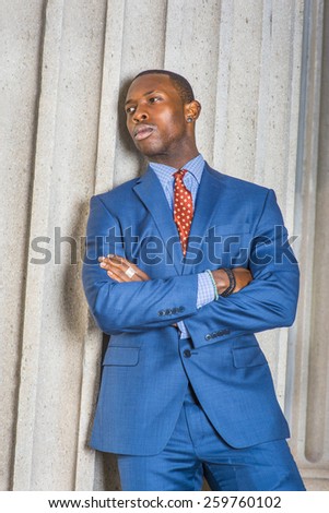Businessman thinking hard. Dressing in blue suit, patterned tie, wearing ear stub, crossing arms, a young black guy standing against column outside office, sad, thinking, lost in thought. Attitude.