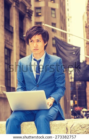 Man working on street. Dressing in blue suit, necktie, a young Japanese Businessman sitting on street in New York, working on laptop computer, looking forward, thinking. Instagram filtered effect.
