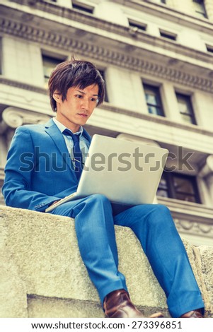 Man working on street. Dressing in blue suit, necktie, a young Japanese Businessman sitting on street in New York, looking down, working on laptop computer. Instagram filtered effect.