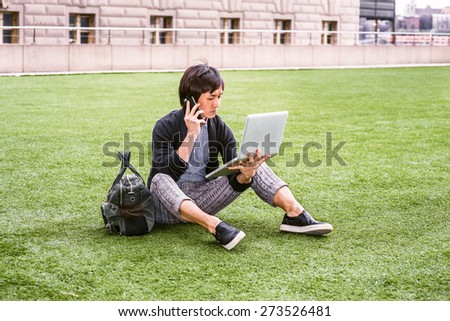 Wearing patterned shirt, black sweater, casual pants, brown leather shoes, carrying bag, a Japanese guy sitting on green lawn, reading, working on laptop computer, making phone call in the same time.