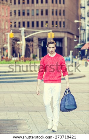 Man Street Fashion. Young blonde guy, wearing red sweater, white pants, fashionable shoes, carrying a hand bag, traveling in New York City. Instagram filtered effect.