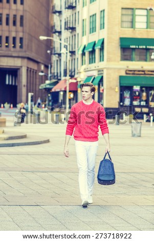 Man Street Fashion. Young blonde guy, wearing red sweater, white pants, fashionable shoes, carrying a hand bag, traveling in New York City. Instagram filtered effect.