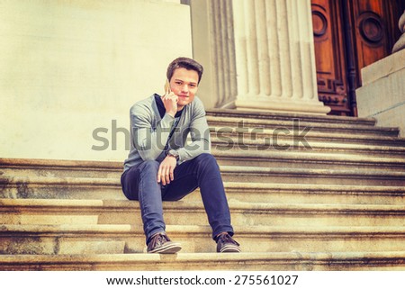 Young Student. Wearing gray V neck cardigan sweater, blue pants, brown sneaker, wristwatch, a young guy sitting on stairs outside office building, smiling, making phone call. Instagram effect.