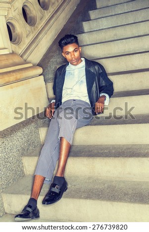 Teenage Fashion. A young,18 years old student, wearing black fashionable leather, wool mixed jacket, striped pants, blue dyed white shirt, leather shoes, sitting on stairs, relaxing. Instagram effect.