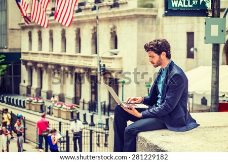 Businessman working on street in New York. Dressing in blue suit, a young guy with beard, sitting outside office building, looking down, reading, typing on laptop computer. Instagram filtered effect.