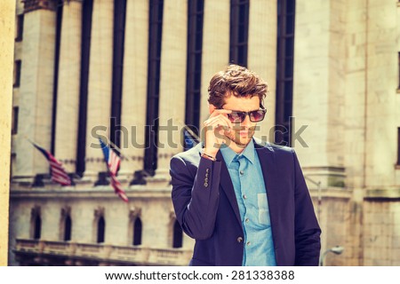 Serious European businessman in New York. Dressing in blue suit, shirt, wearing sunglasses, a young handsome guy with beard standing in business district, looking down, thinking. Instagram effect.