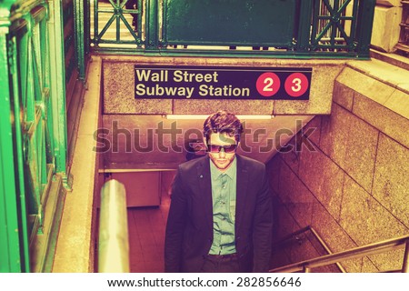 Retro filtered look. Wearing sunglasses, looking down, young serious businessman walking on stairs, going out from underground subway station on Wall Street  in New York, thinking, tough work ahead.