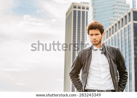 The skyÃ¢Â?Â?s the limit. Man Power. Wearing leather jacket unbuttoned,  a young handsome businessman with beard, standing in business district, looking down, thinking. Instagram effect. Copy Space