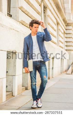 Serious European college student studying in New York. Wearing blue blazer, jeans, sneakers, holding a laptop computer, hand touching hair, a young guy walking on campus, thinking. Instagram effect.