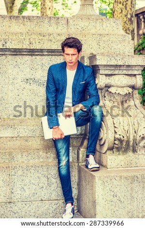Serious European college student studying in New York. Wearing blue blazer, jeans, sneakers, holding a laptop computer, a young guy standing at the corner on campus, thinking. Instagram effect.