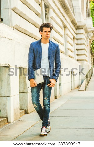 Serious European college student studying in New York. Wearing blue blazer, jeans, sneakers, hands holding a laptop computer, a young guy walking on campus, thinking. Casual Fashion. Instagram effect.