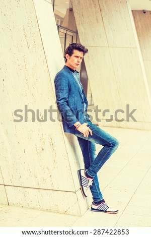 Man Casual Urban Fashion. Wearing blue blazer, patterned under shirt, jeans, fashionable sneakers, a young European college student standing against column outside office building. Instagram effect.