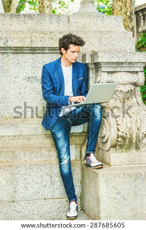 European college student studying in New York. Wearing blue blazer, jeans, sneakers, a young guy staying at quiet corner on campus, reading, typing, working on laptop computer. Instagram effect.