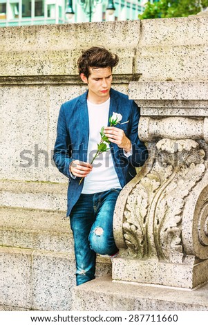 European college student seeking love in New York. Wearing blue blazer, jeans, a young guy standing at corner against wall on campus, holding white rose, thinking, missing you. Instagram effect.