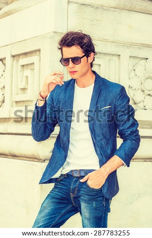 Man Casual Fashion. Dressing in blue blazer, white under shirt, jeans, wearing sunglasses, a young European college student standing on campus in New York, hand stopping in air, thinking.
