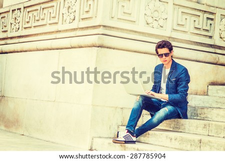 European college student studying in New York. Wearing blue blazer, jeans, sneakers, sunglasses, young guy sitting on stairs on campus, reading, thinking, working on laptop computer. Instagram effect.