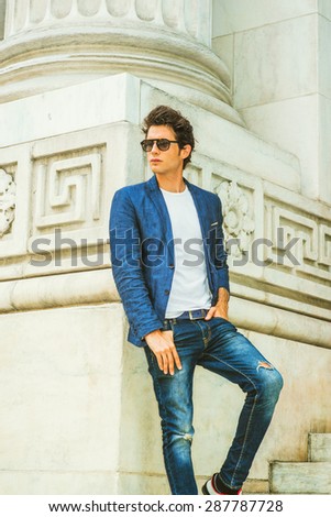 Man Casual Fashion. Dressing in blue blazer, white under shirt, jeans, wearing sunglasses, a young European college student standing by column on campus in New York, looking away. Instagram effect.