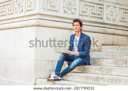 European college student studying in New York. Wearing blue blazer, jeans, sneakers, a young guy sitting on stairs on campus, reading, thinking, working on laptop computer, confidently looking up.