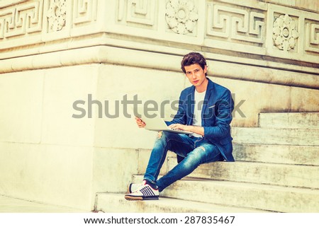 European college student studying in New York. Wearing blue blazer, jeans, sneakers, a young guy sitting on stairs on campus, reading, thinking, working on laptop computer. Instagram filtered effect.