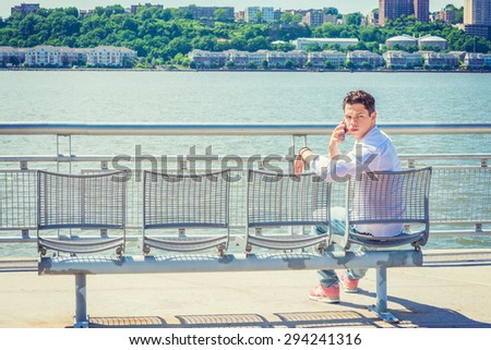 Empty Chairs for You. Wearing white shirt, jeans, sneakers, a young lonely guy sitting by Hudson River in New York, facing New Jersey, head turning back, making phone call, waiting for you. Copy Space