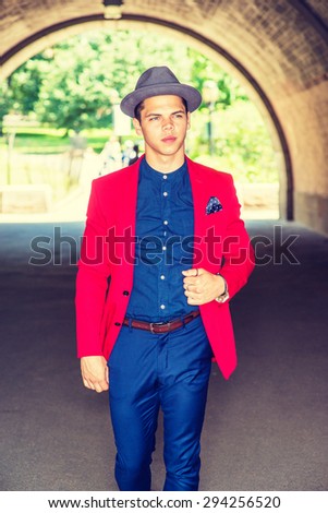 Businessman traveling in New York. Dressing in red blazer, blue collarless shirt, pants, wearing Fedora hat, a young guy walking through under bridge, confidently looking forward. Instagram effect.