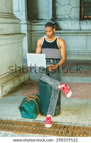 College student traveling, working in New York. Wearing black, white striped tank top, jeans, red sneakers, carrying green bag, a black guy sitting on street, reading, working on laptop computer.