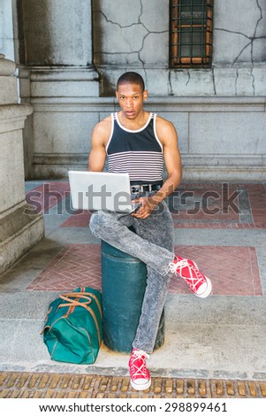 College student traveling, working in New York. Wearing black, white striped tank top, jeans, red sneakers, carrying green bag, a black guy sitting on street, reading, working on laptop computer.