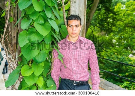 Man casual fashion. Wearing red, white patterned, long sleeve shirt, a young guy standing by green plants with big leaves, thinking, lost in thought. Concept of environment protection. Love Green.