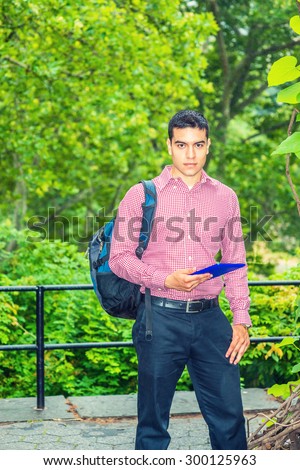 Back to School. Wearing patterned shirt, carrying shoulder bag, hand holding tablet computer, a college student standing by woods on campus, confidently looking forward. Fog, drizzle on background.