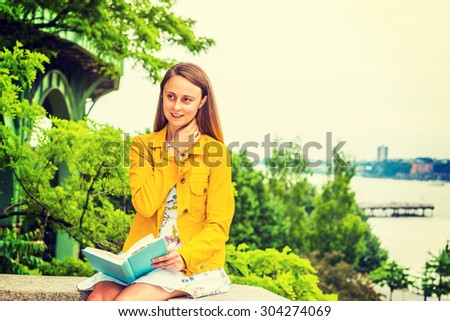 American college student studying in New York. A girl wearing flower patterned underdress, yellow corduroy jacket, holding green book, sitting by Hudson River, reading, thinking. Instagram effect.