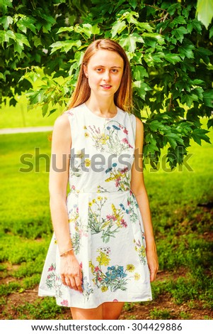 Summer Green. Wearing flower patterned, sleeveless, white dress, an American college student stranding on green lawn by trees on campus, smiling, looking at you. Concept of Environment Protection.