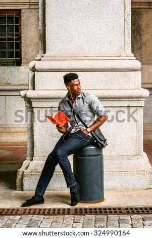 African American College Student studying on street in New York, wearing gray shirt, jeans, cloth shoes, wristwatch, carrying shoulder leather bag, listening music with earphone, reading red book.