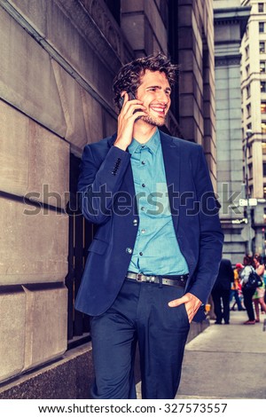 European businessman traveling in New York. Young guy with beard walking through crowded high building street, talking on mobile phone, smiling, excited with good news. Technology in Daily Life.