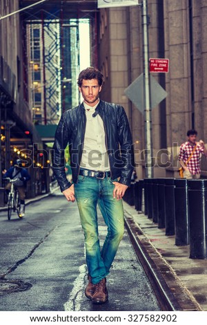 European businessman traveling in New York. Wearing black leather jacket, white undershirt, blue jeans, brown boot shoes, a young guy with beard walking on narrow wet street after raining,