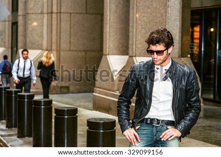 Man Casual Street Fashion. Dressing in black leather jacket, blue jeans, wearing sunglasses, a young European Businessman with beard sitting on street in New York, looking down, thinking, relaxing.