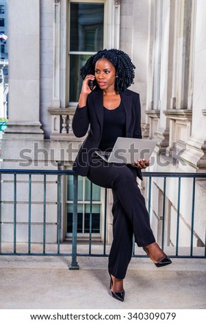African American Businesswoman working in New York. Young black college student sitting on railing in office building, working on laptop computer, making phone call. Filtered look with dark blue tint.