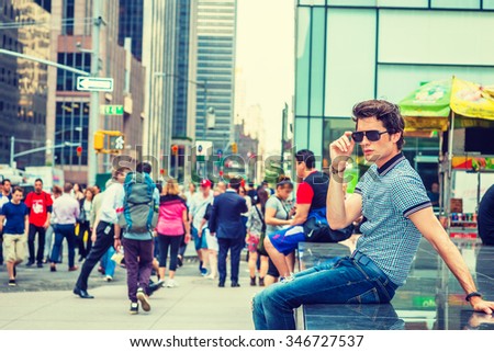 European college student traveling in New York. Wearing blue pattered short sleeve shirt, holding sunglasses, a guy sitting on street, thinking. Many people on background. Instagram filtered look.