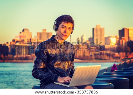 Asian American college student traveling, studying in New York, wearing black leather jacket, headphone, sitting by river in sunset, listening music, working on laptop computer. Instagram effect.