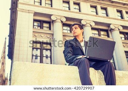 Power of Modern Technology. East Indian American college student traveling, studying in New York, sitting on street outside office building, working on laptop computer. Instagram filtered effect.